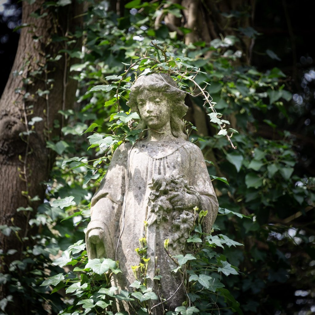 Mädchen-Statue von Efeu umwuchert.